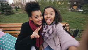 Two women taking a selfie outdoors on a bench.